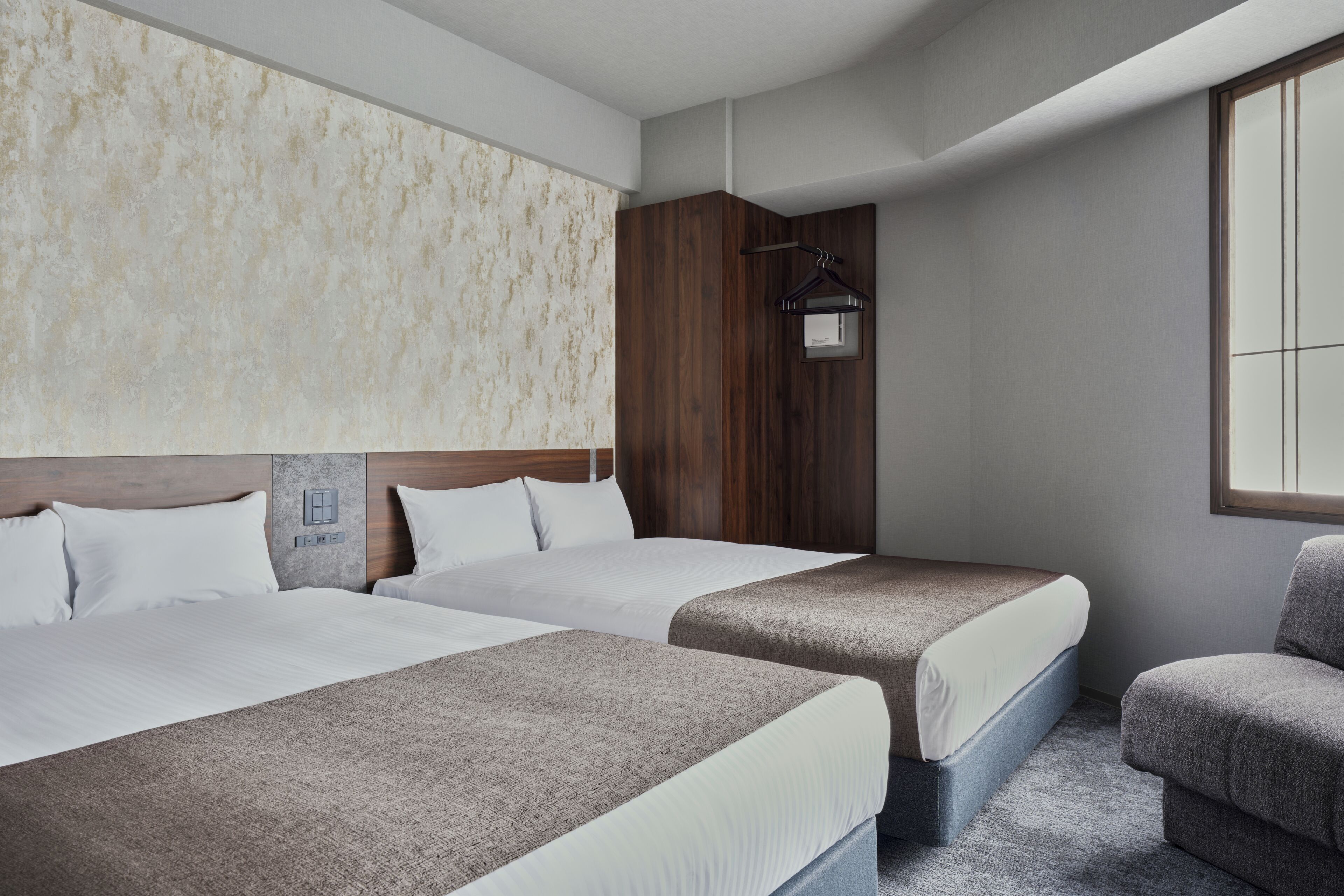 A hotel room with two beds, a wooden headboard, a hanging light fixture, and a window.