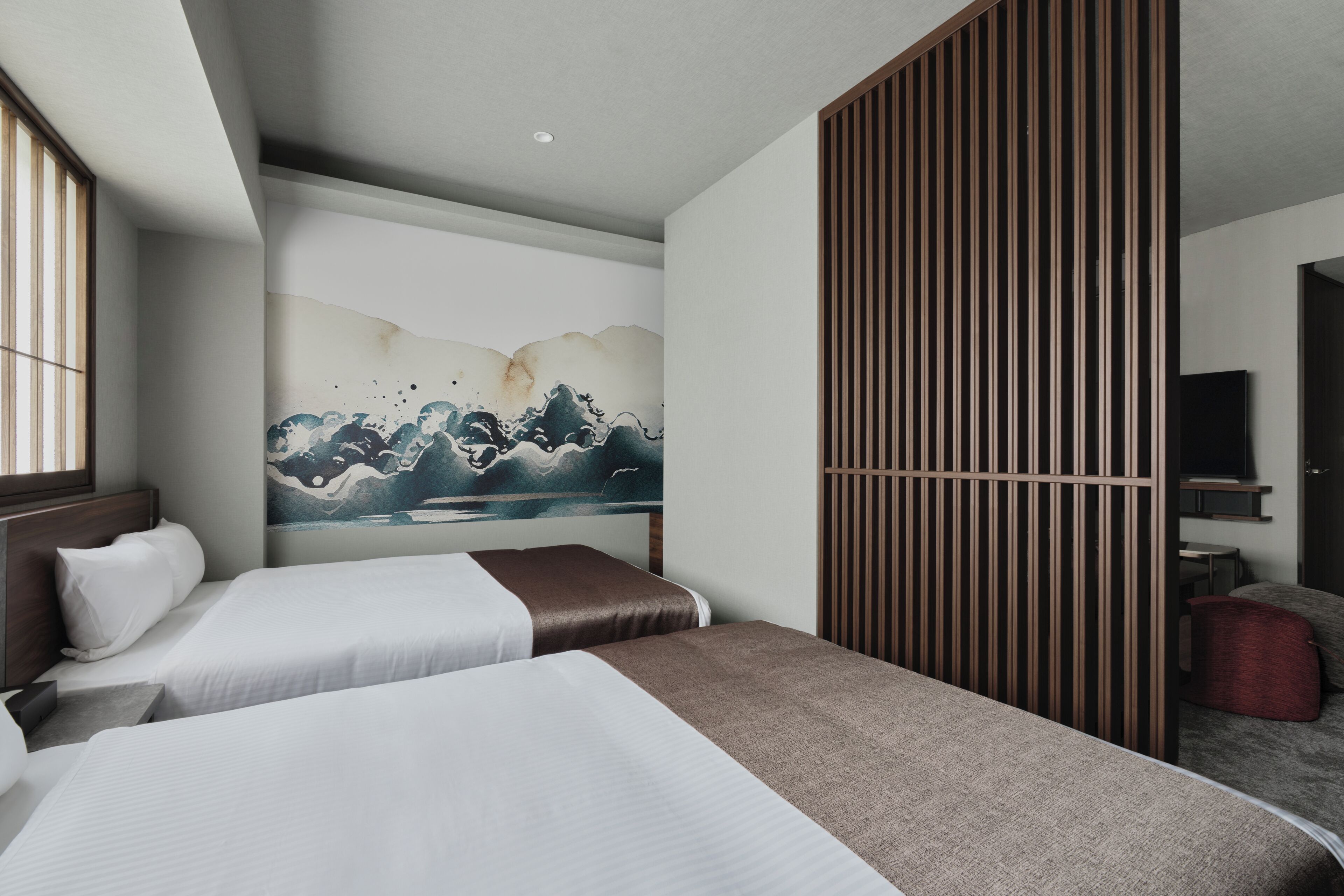 Quarto de hotel com duas camas, uma pintura grande de ondas, uma porta de correr e uma televisão.