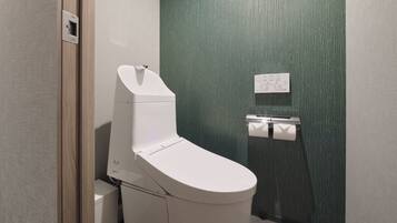 A modern bathroom with a white toilet, a paper towel dispenser, and a green textured wall.