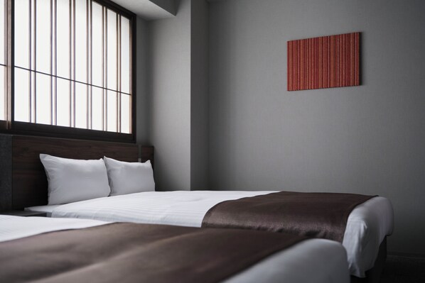 A modern hotel room with a large bed, a window with blinds, and a red accent wall.