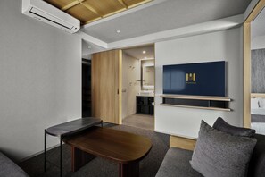Una habitación de hotel moderna con televisión de pantalla plana, una mesa de madera, un sofá y una puerta corredera que da a un baño.