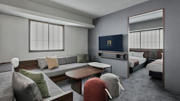 A modern hotel room with a sofa, a small table, a TV, and a bed.