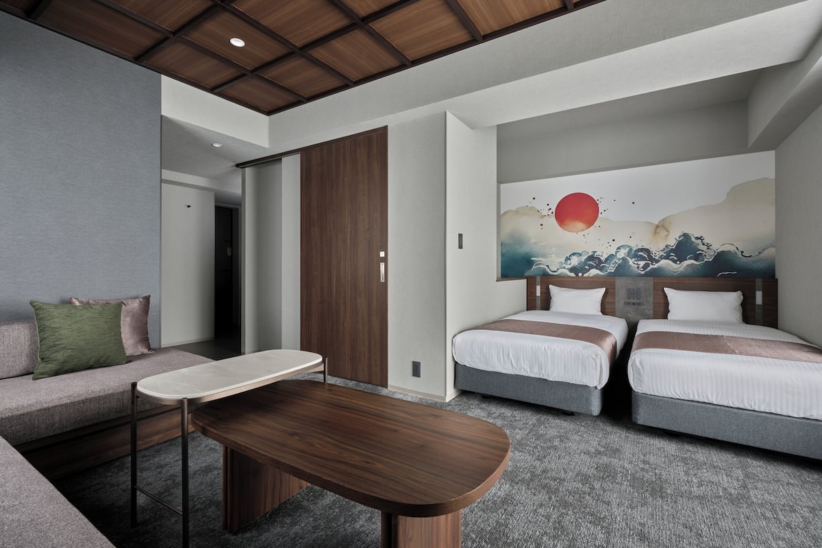 Una habitación de hotel moderna con un sofá, dos camas, un cuadro y una mesa de madera.