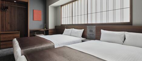 A hotel room with two beds, a wooden wardrobe, a small table, and a large window with vertical blinds.