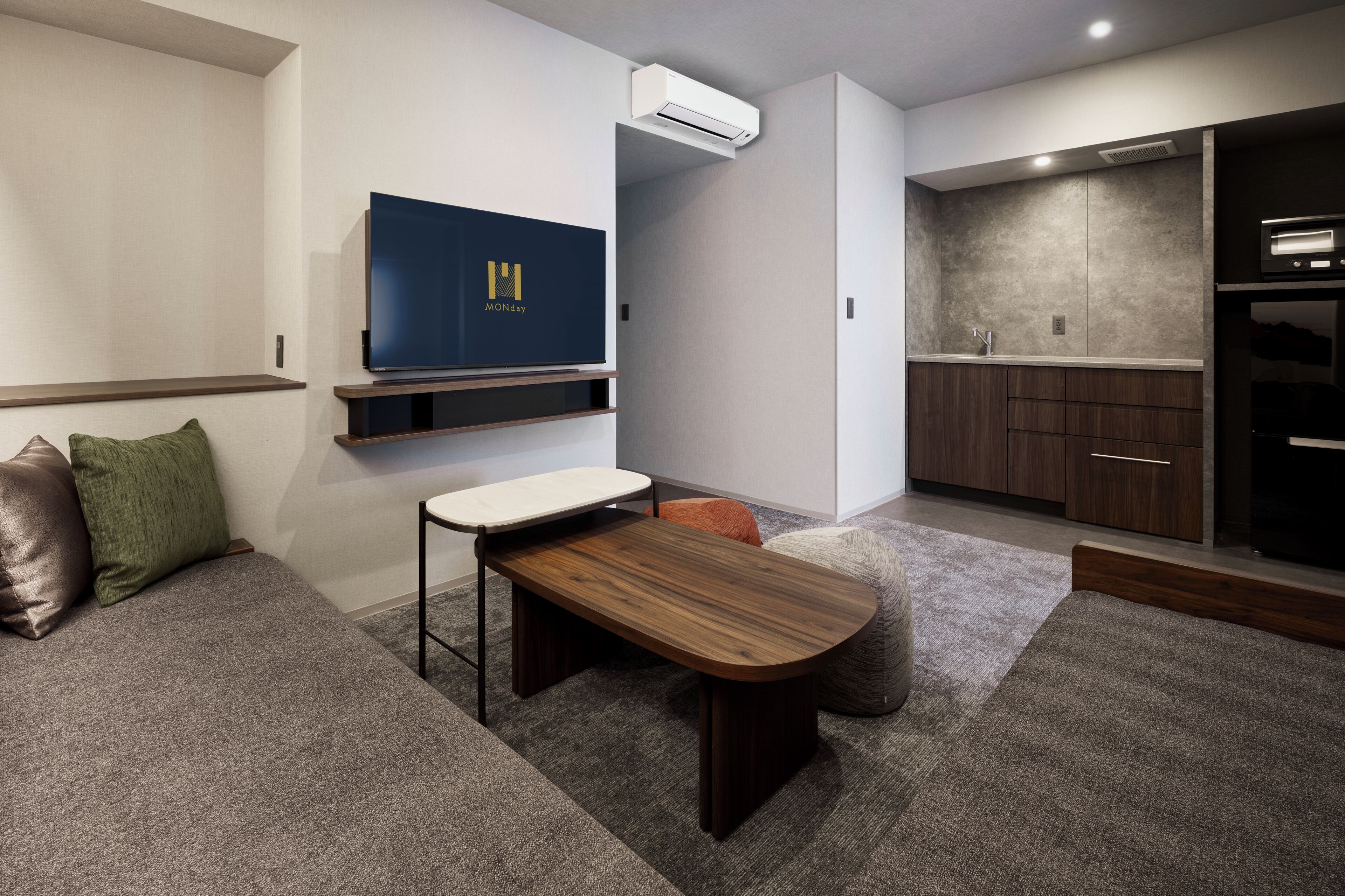 Una sala de estar moderna con una televisión de pantalla plana, un banco de madera, un sofá y una zona de cocina con armarios y encimera.