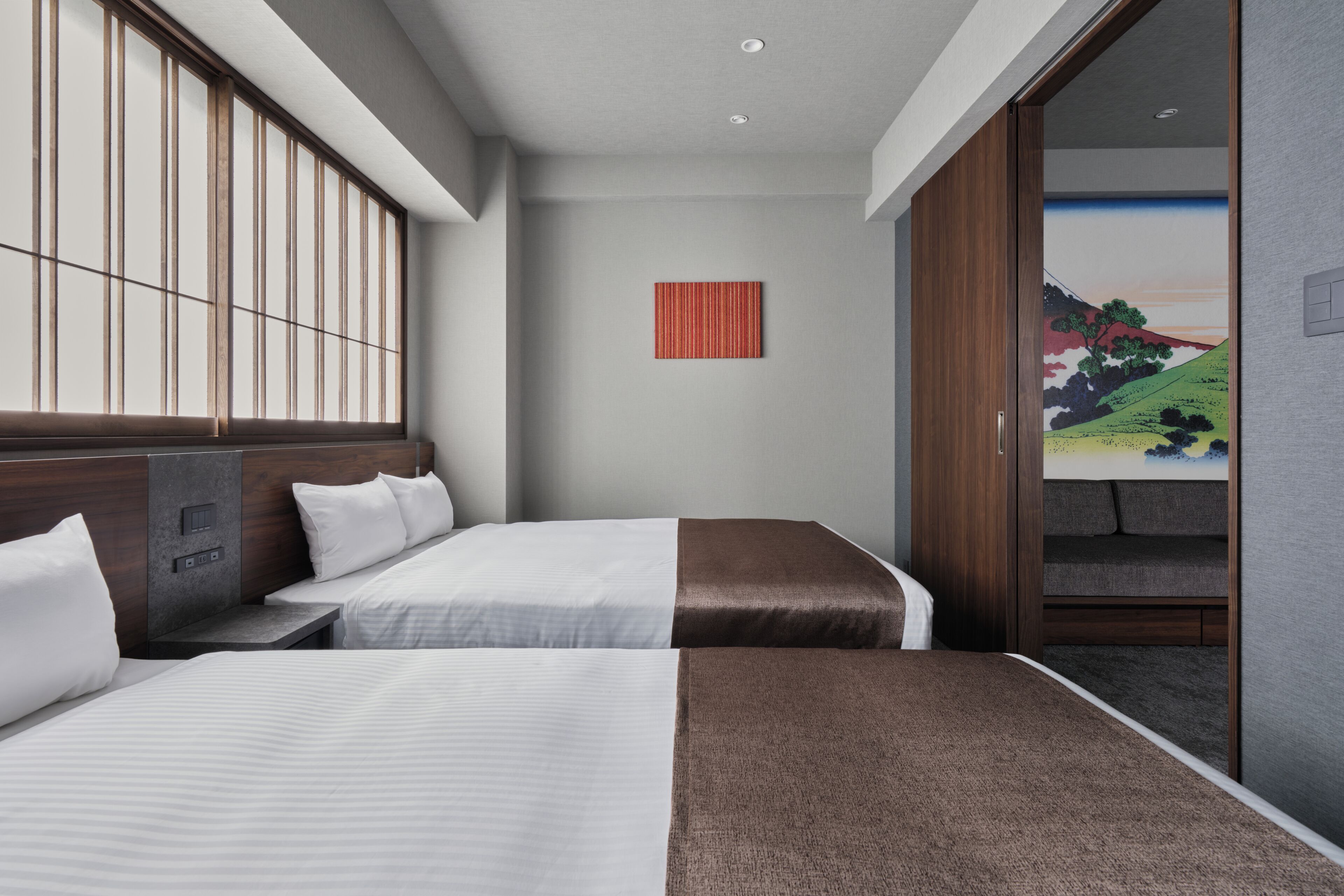 Habitación de hotel con dos camas, cabecero de madera, una obra de arte roja en la pared y vista a un paisaje por una puerta abierta.