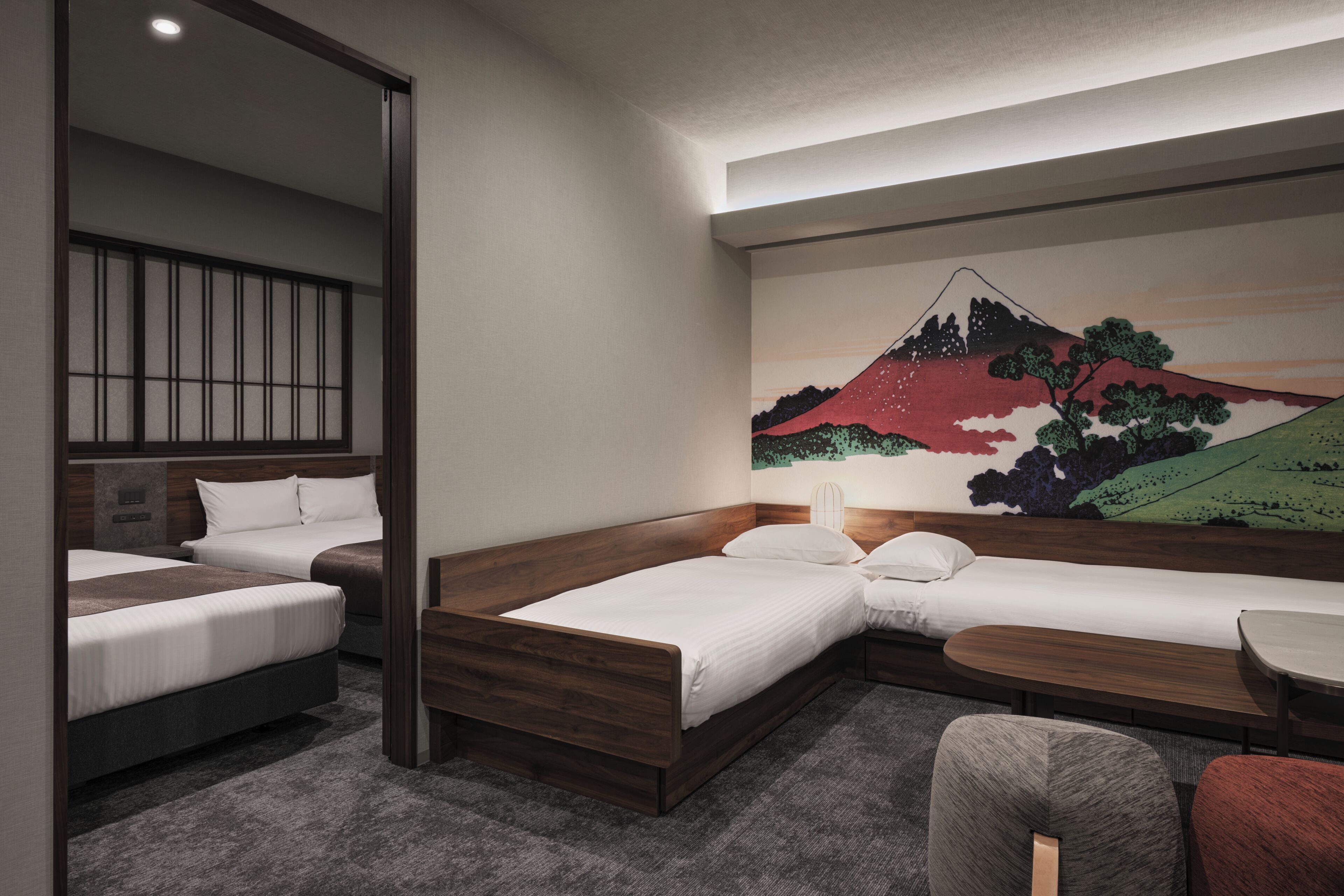 A hotel room with two beds, a sofa, a small table, and a wall mural of a mountain.