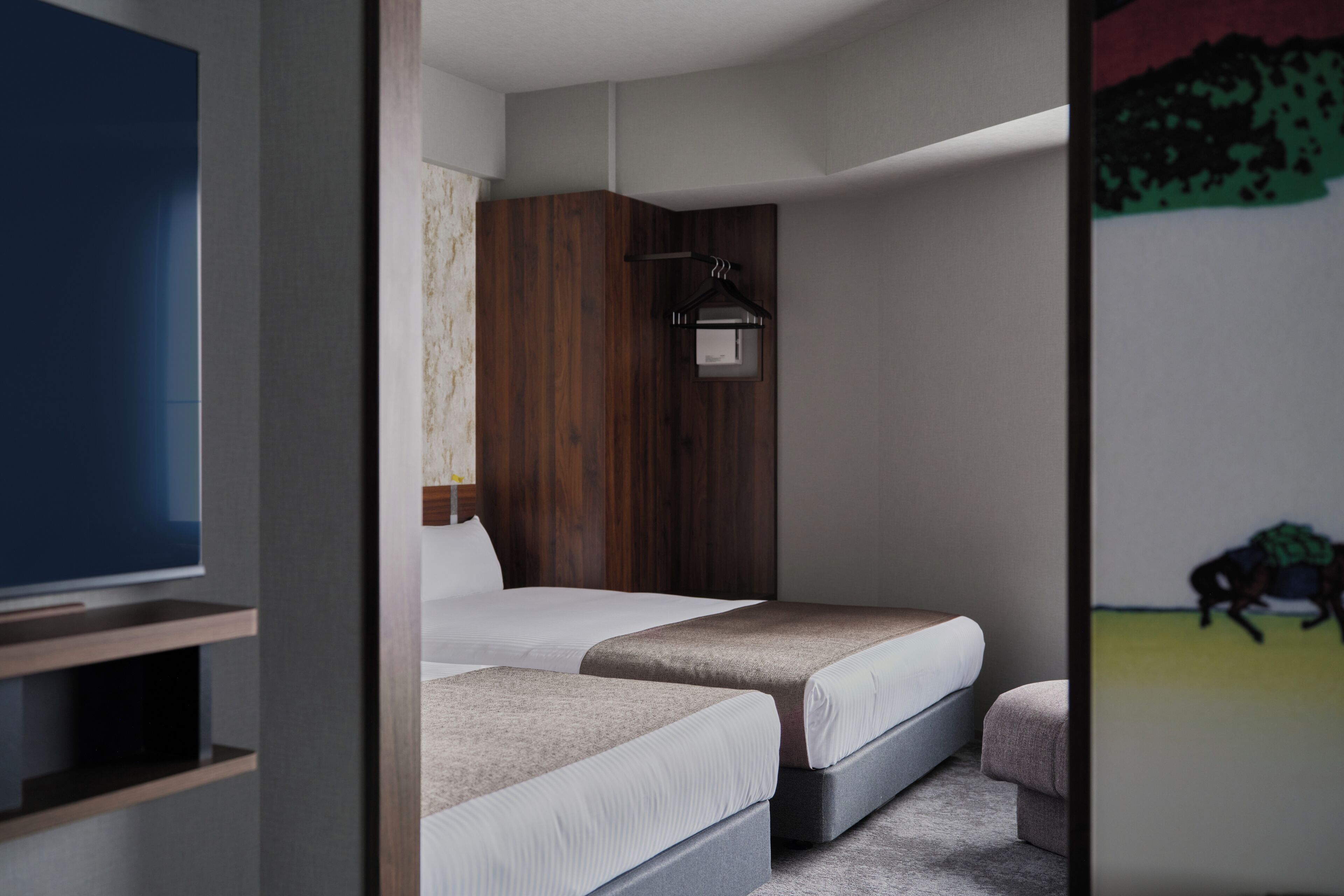 Une chambre avec deux lits, une armoire en bois, une télévision et un mur orné d’un tableau.