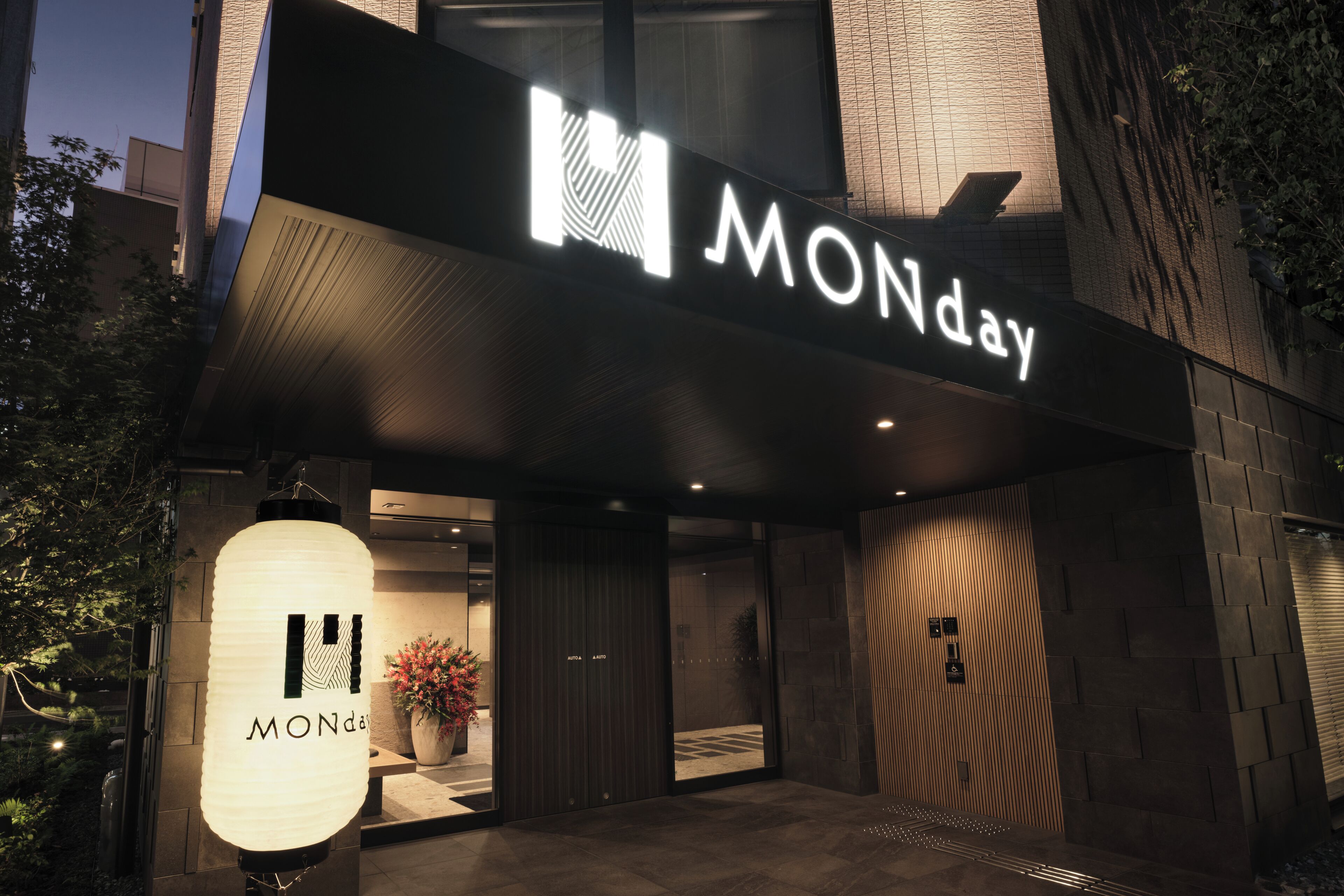 Un edificio moderno con un llamativo letrero 'MONday', una planta grande en maceta y una pared texturizada.