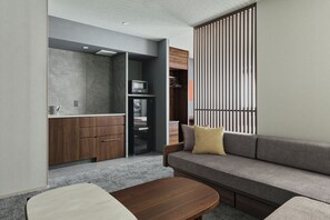 Una sala de estar moderna con sofá, una mesa de centro y una zona de cocina con armarios y electrodomésticos.