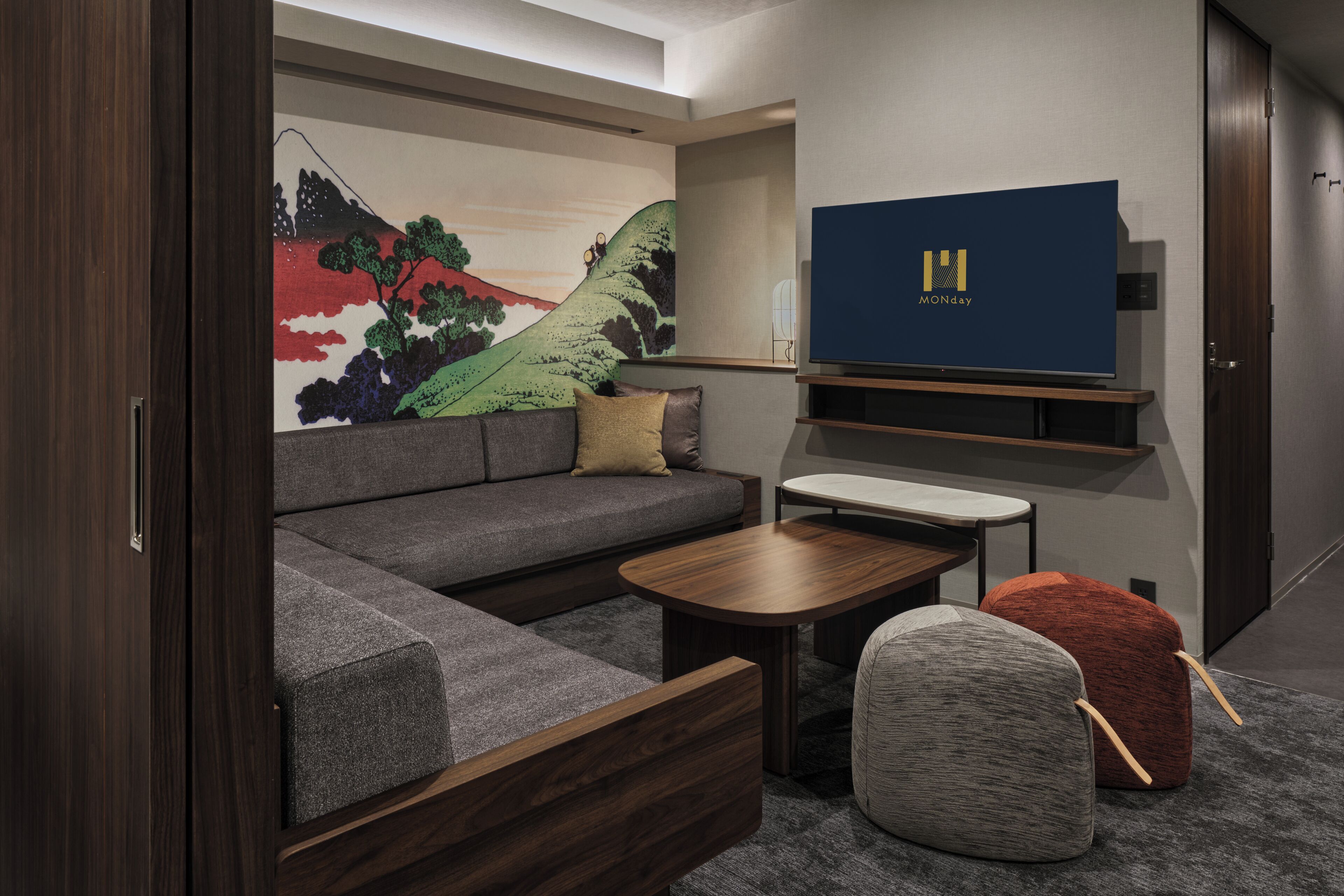 A modern living room with a sectional sofa, a flat-screen TV, a small table, and a colorful wall mural.