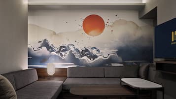 A modern living room with a sofa, a small table, and a wall mural depicting a sunset over mountains.