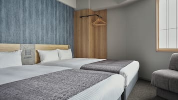 A hotel room with two beds, a wooden headboard, a grey carpet, a grey armchair, and a wooden wardrobe.