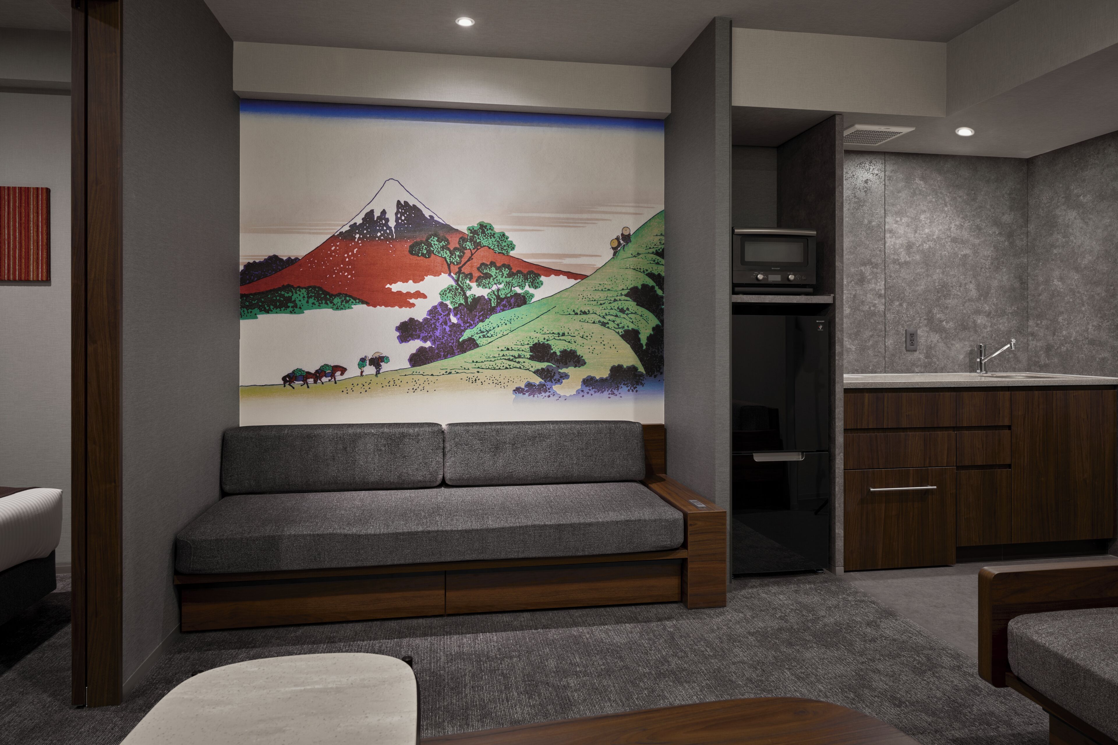 A modern interior with a grey sofa, wooden cabinets, and a wall-mounted artwork of a mountain scene.