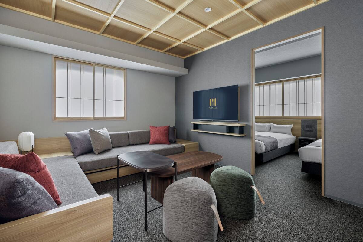 Una habitación de hotel moderna con sofá, una mesita, una silla, cama, televisión y espejo.