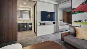 A modern hotel room with a wooden wardrobe, a sofa, a TV, a painting, and a bathroom with a mirror and sink. - Premium MONday ASAKUSA I (Tokyo)