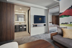 A modern hotel room with a wooden wardrobe, a sofa, a TV, a painting, and a bathroom with a mirror and sink. - Premium MONday ASAKUSA I (Tokyo)