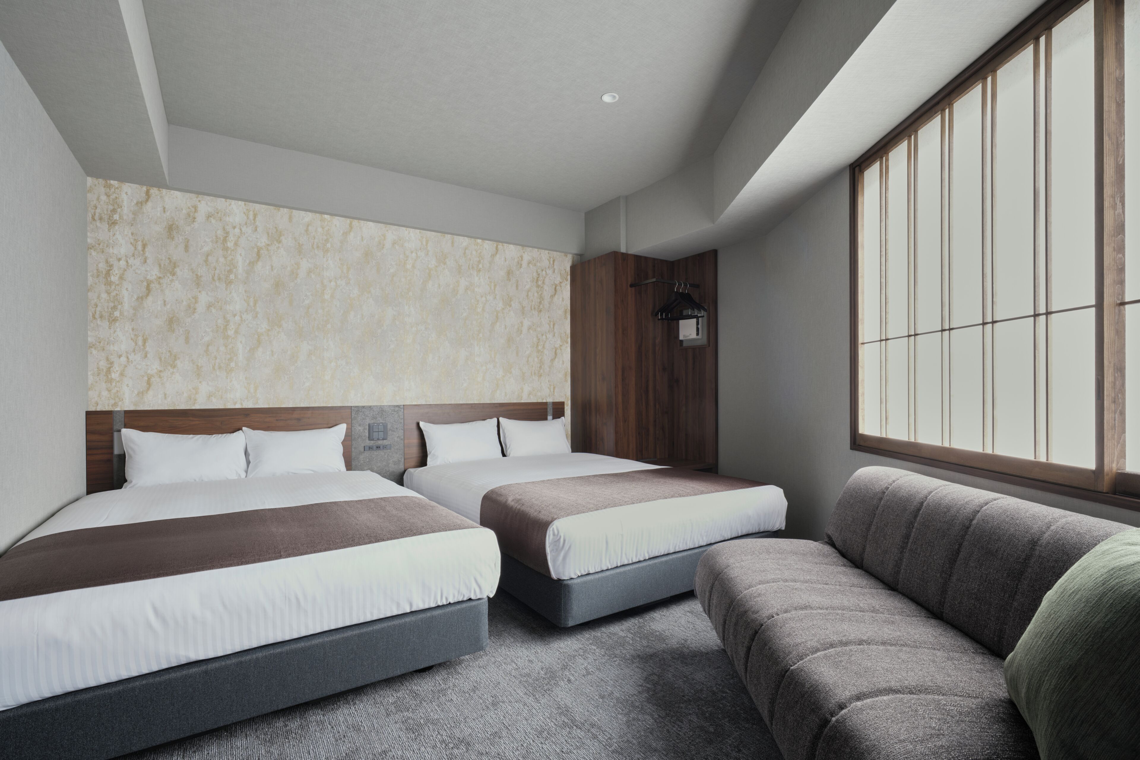 A hotel room with two beds, a sofa, a large window, and a wooden headboard.