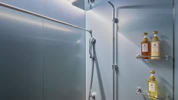 A modern shower with a handheld showerhead and a rain shower head, two soap dispensers on a glass shelf, and a metal grab bar.