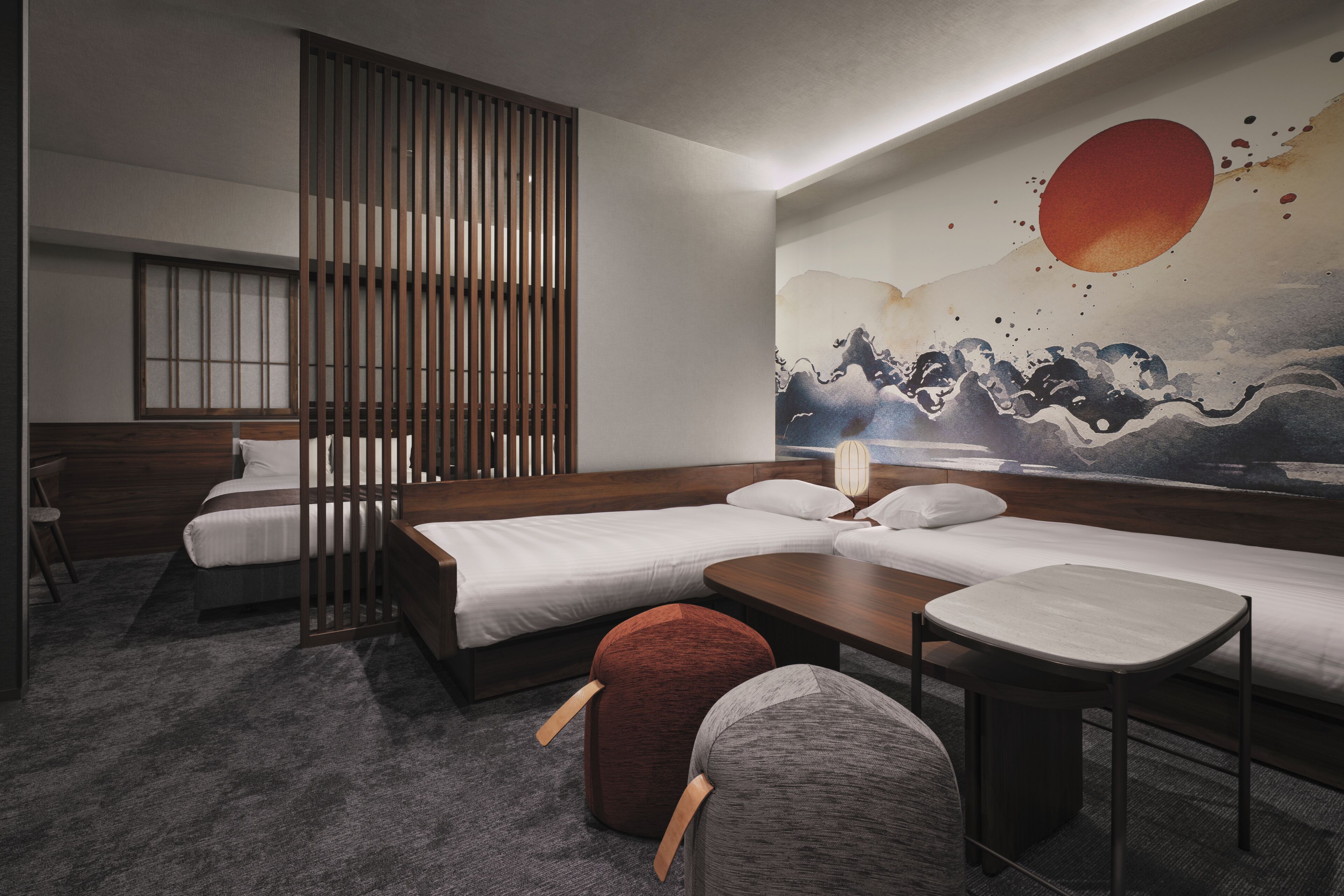 A hotel room with two single beds, a wooden partition, a mural, and a small seating area.