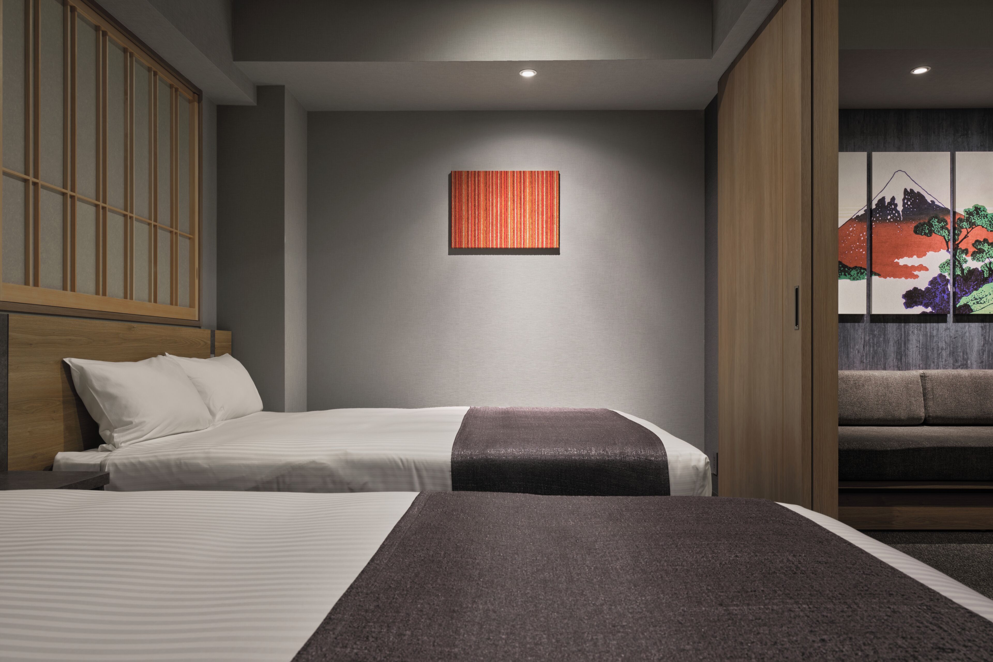 A hotel room with two beds, a wooden wardrobe, a wall-mounted artwork, and a sliding door with a view of a mountain.