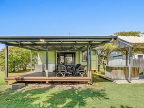 Ein überdachter Sitzbereich im Freien mit Tisch und Stühlen, ein eingezäunter Garten und ein Haus im Hintergrund.