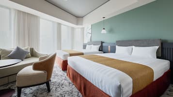 Quarto de hotel com uma cama, duas poltronas, uma mesa pequena e uma janela grande com cortinas.