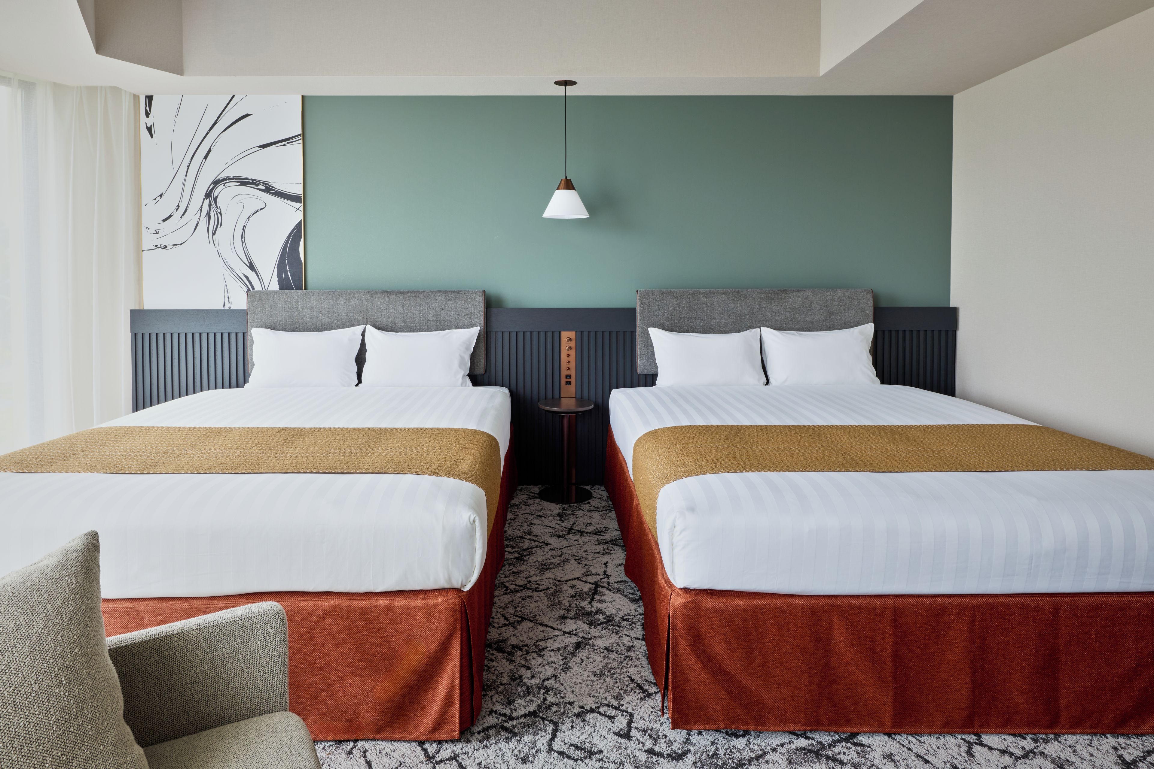 A hotel room with two beds, a wall-mounted artwork, a pendant light, and a patterned carpet.