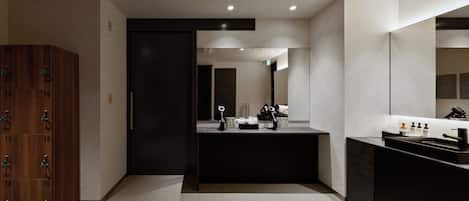 Un baño moderno con un mueble de madera oscura, un lavamanos con espejo y un espejo grande sobre el lavamanos.