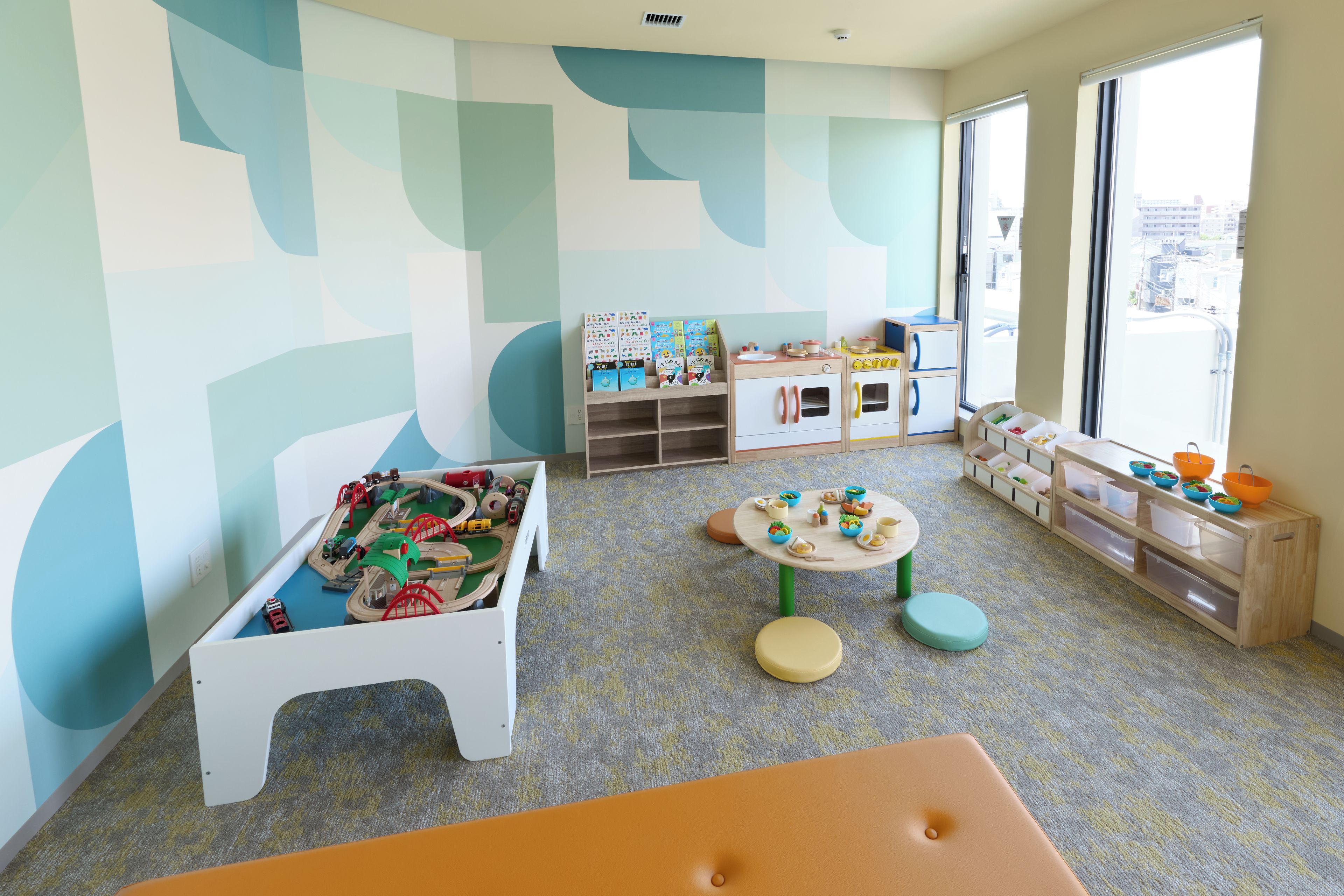 A children's playroom with a train set, play tables, and storage units.
