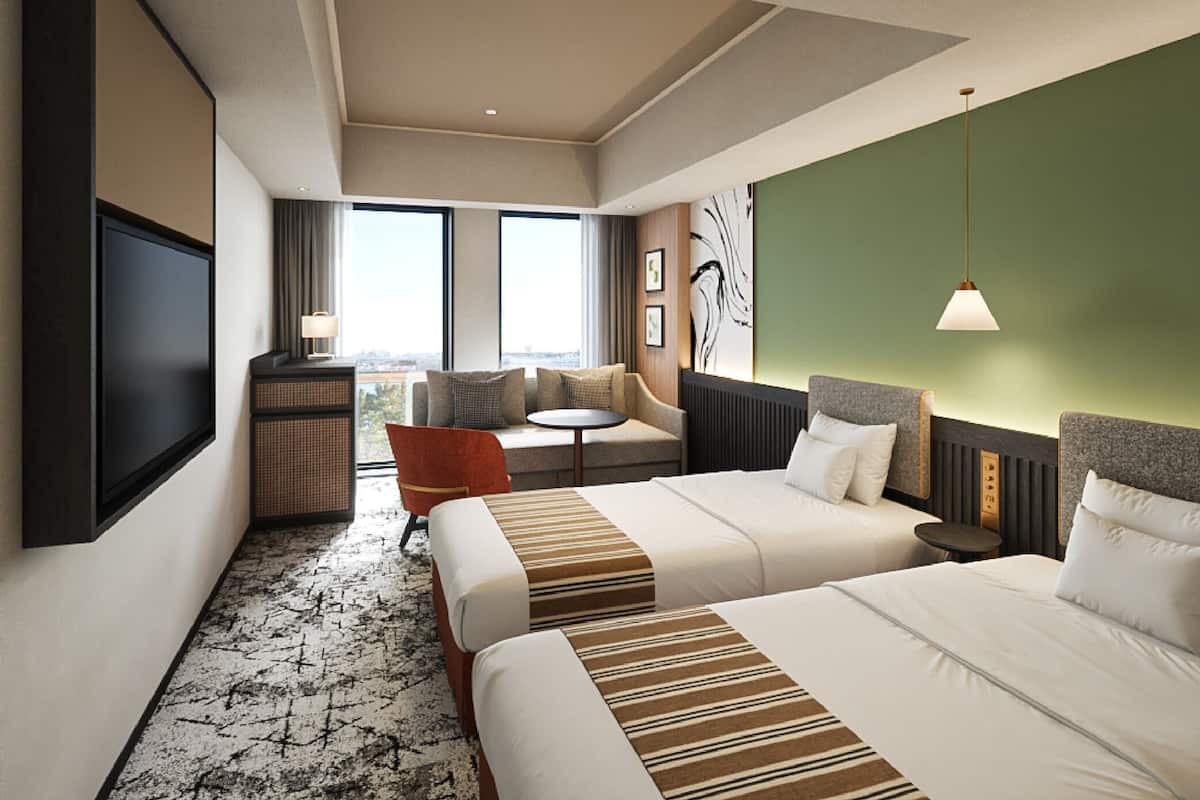 Habitación de hotel con dos camas, un sofá, un televisor, un escritorio y vistas a la ciudad.