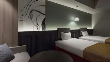 Quarto de hotel com duas camas, uma mesa redonda, um sofá e uma parede decorada com arte abstrata.