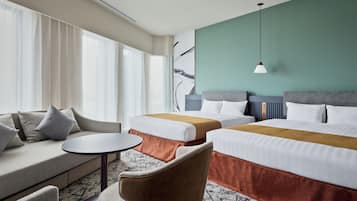 A hotel room with a sofa, two beds, a small table, and a chair.