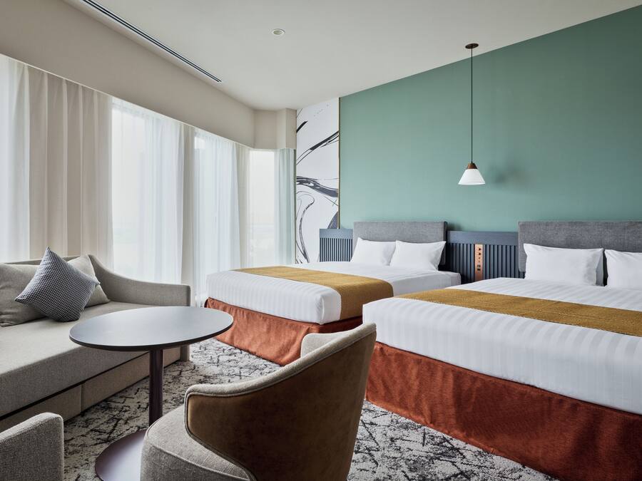 A hotel room with a sofa, two beds, a small table, and a chair.
