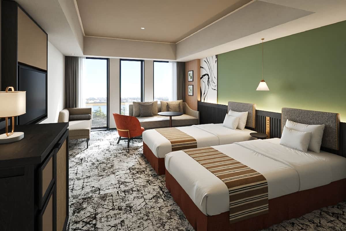 Habitación de hotel con dos camas, un escritorio, una silla, un sofá y ventanas grandes.