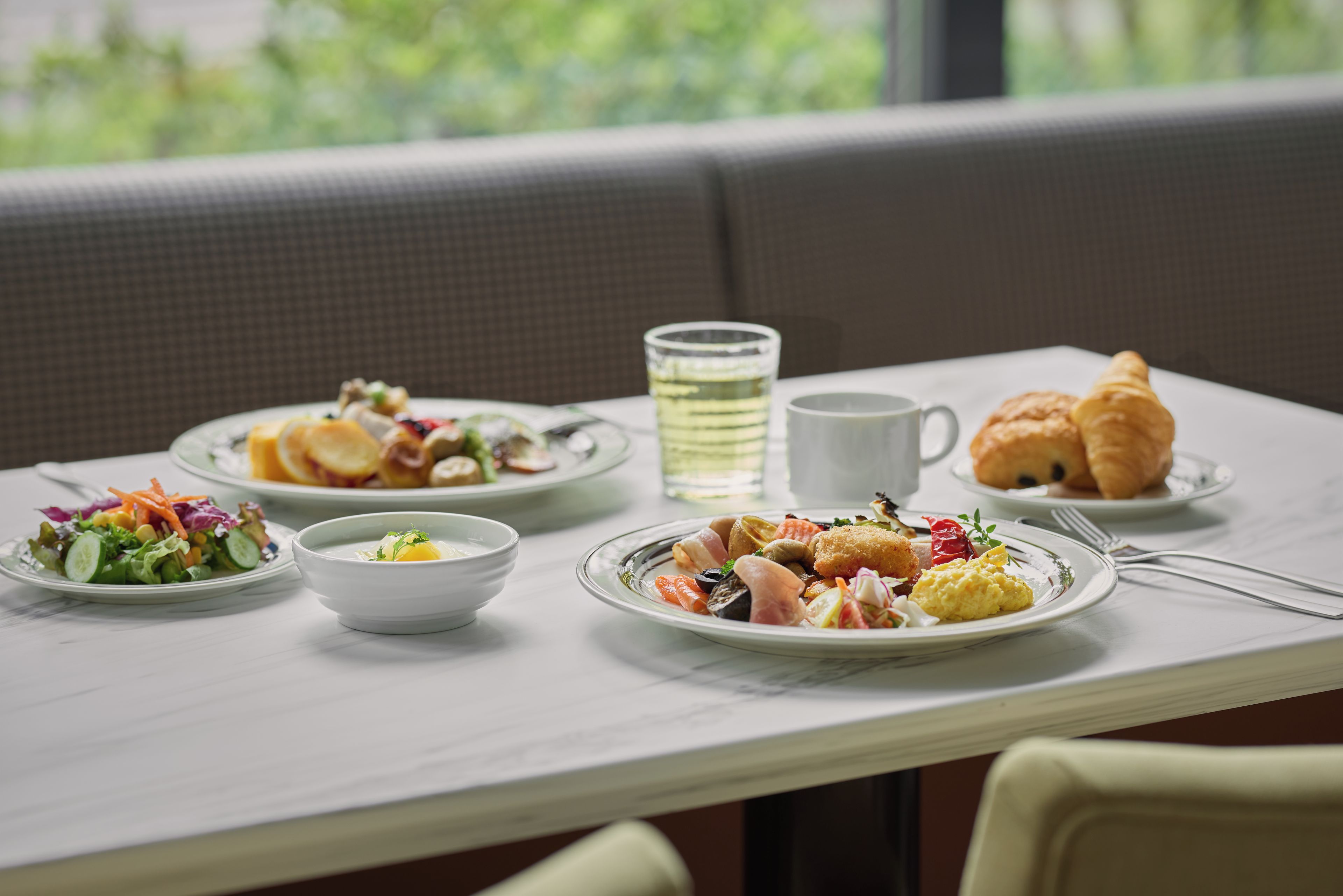 Una mesa de comedor con platos de comida, un vaso de agua y un croissant.
