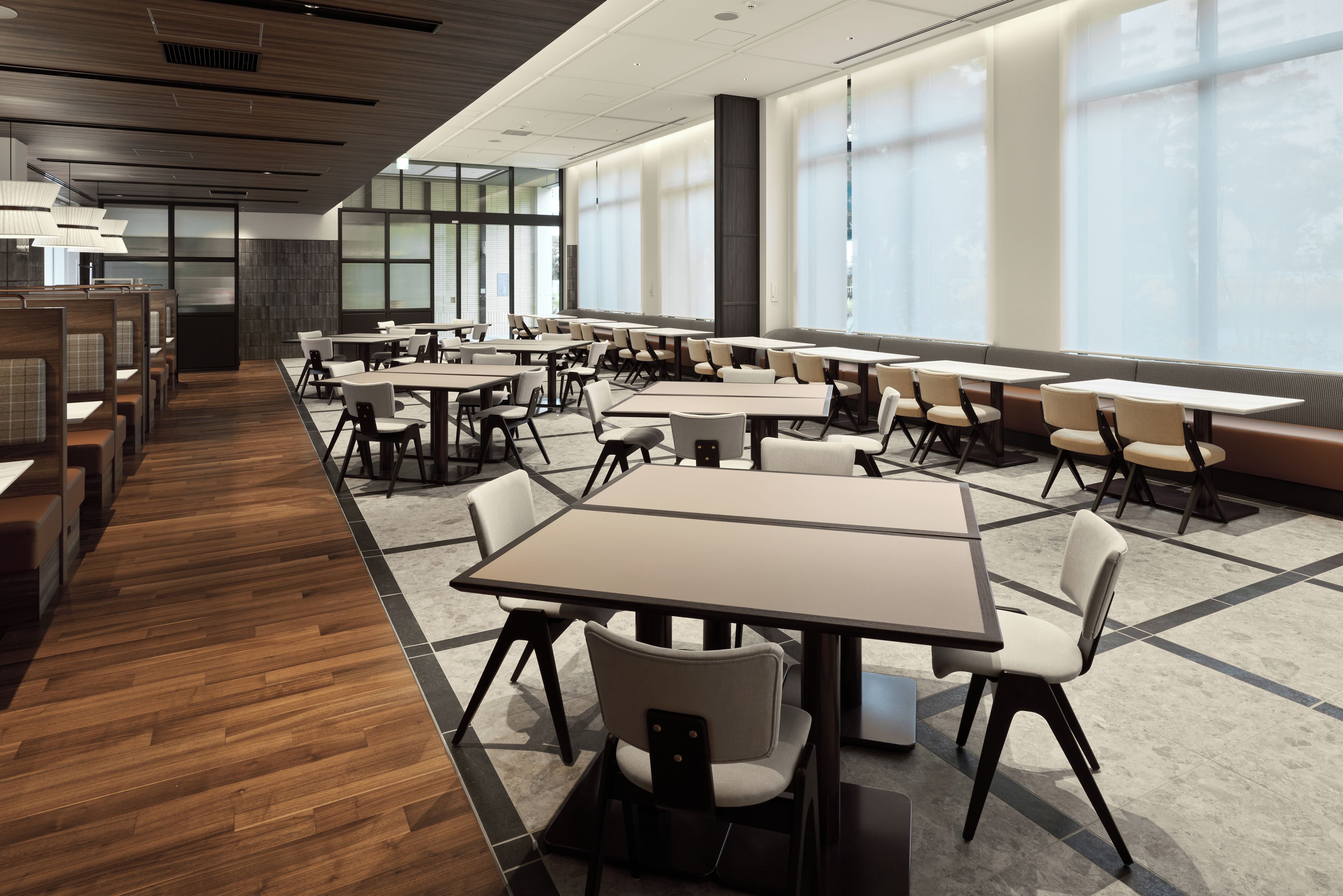 A modern conference room with multiple tables and chairs, large windows, and a wooden floor.