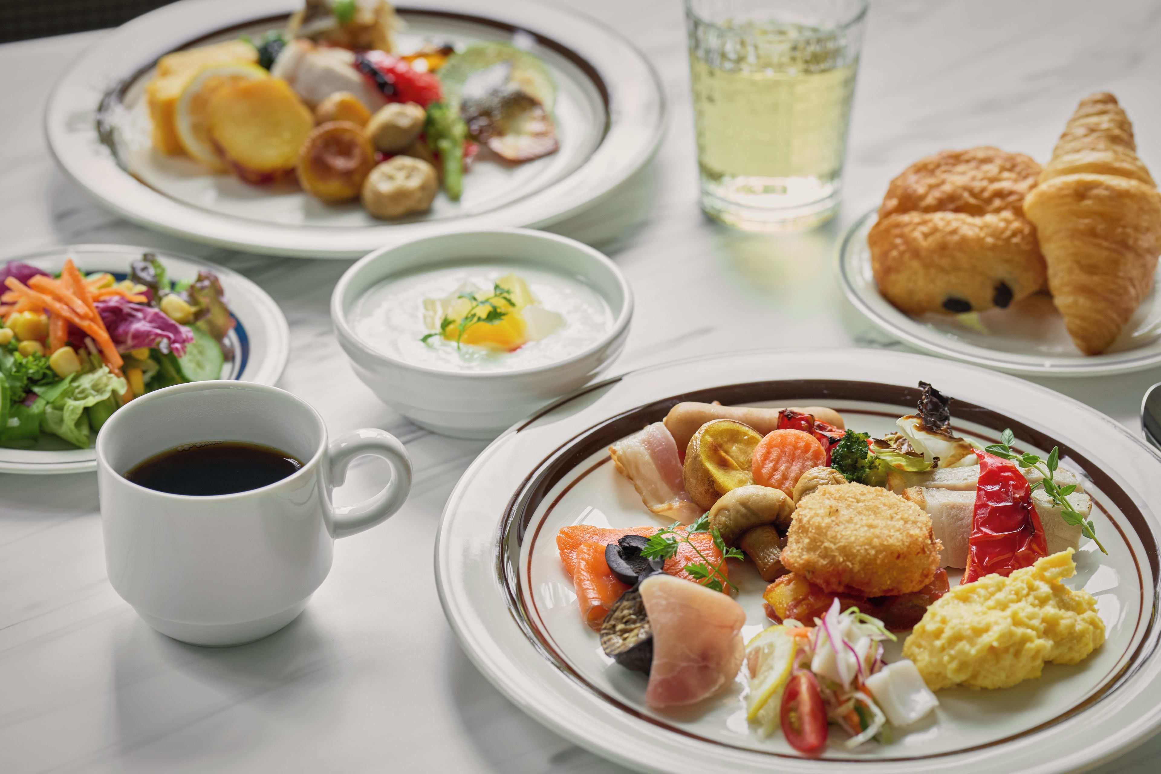 A table set with various dishes, a glass of beverage, and a croissant.