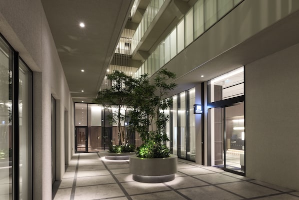 A modern hotel corridor with glass doors, potted plants, and a tiled floor.
