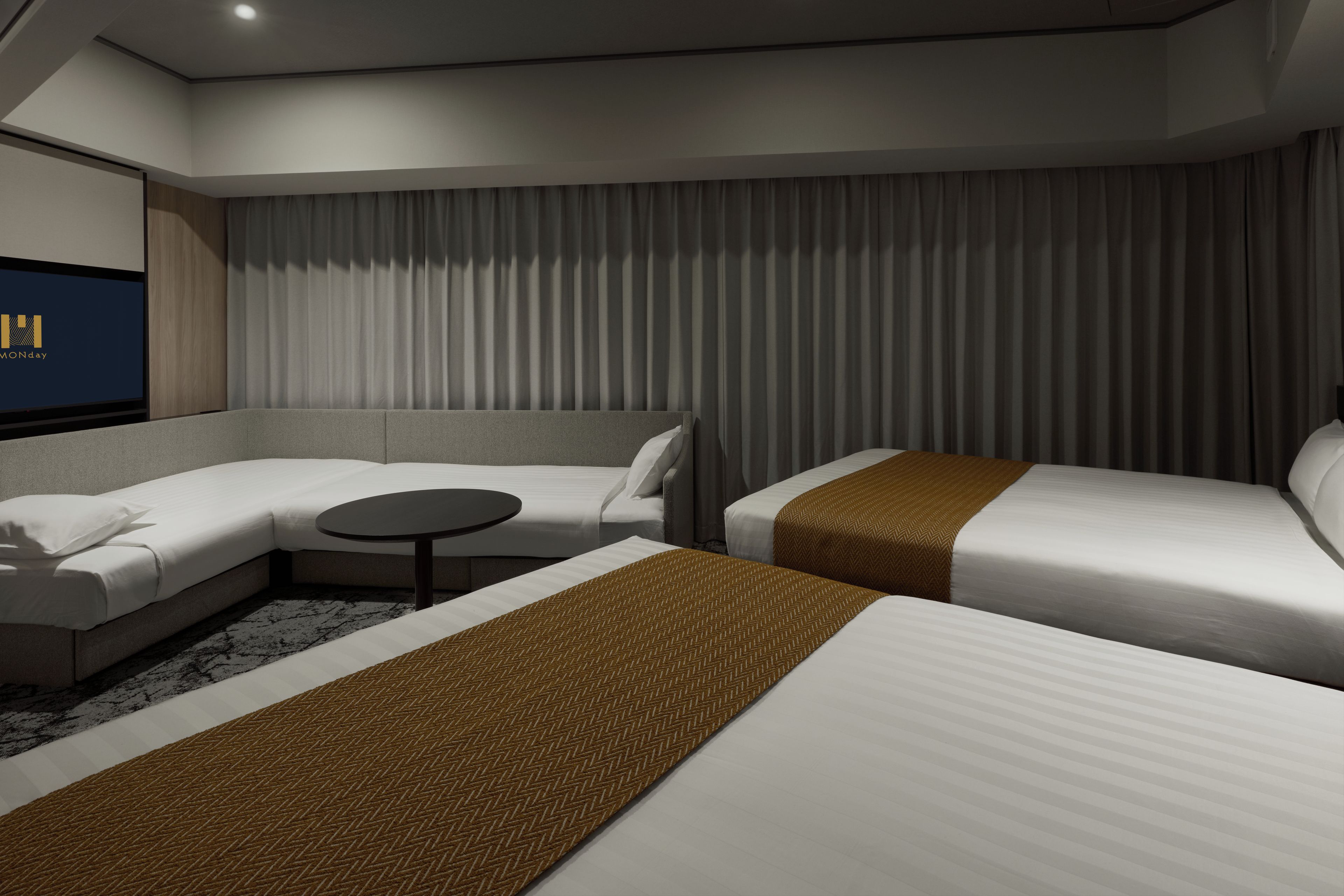 A modern hotel room with a sofa, a single bed, a small table, and a television.