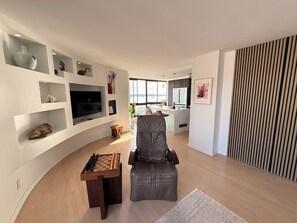 Un salon moderne doté d’un téléviseur à écran plat, d’une table d’échecs, d’un fauteuil en cuir et offrant une vue sur l’extérieur.
