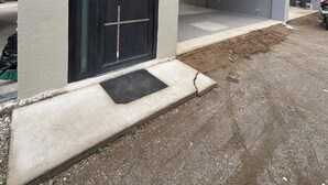 En modern byggnad med en stor svart dörr, en entré i betong och en asfalterad uppfart.