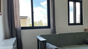 Ett rum med en grön soffa, ett vitt skrivbord och ett fönster med gardiner.