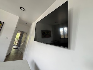 A hallway with a large flat-screen TV mounted on the wall, a door leading to a balcony, and a light switch on the wall.