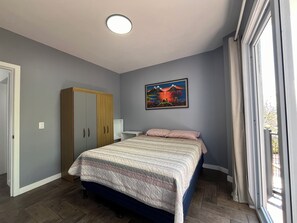 A bedroom with a bed, a wardrobe, a painting, and a window.