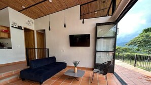 A modern living area with a sofa, a small table, a chair, a TV, and a balcony with a view. - Casa Campestre San Joaquin La Mesa (La Mesa)