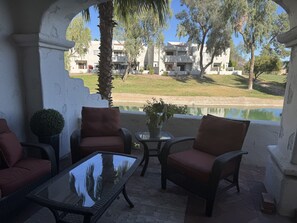 An outdoor seating area with wicker furniture and a glass table, overlooking a body of water and buildings. - Arizona Biltmore area Premier 2-bedroom condo (Phoenix)
