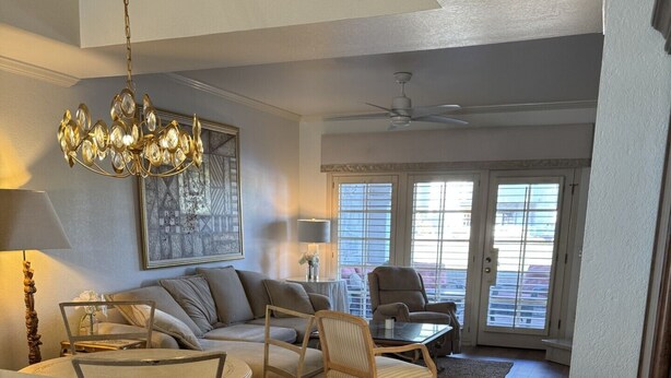 Ein Wohnzimmer mit Sofa, Sesseln, einem Couchtisch, einer Chandelier und einer Tür, die auf einen Balkon führt.