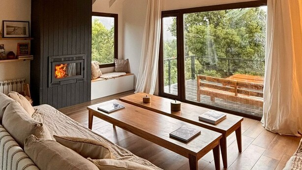 Une chambre confortable aménagée en mezzanine, avec une cheminée, un canapé, une table à manger et de grandes fenêtres donnant sur l’extérieur.
