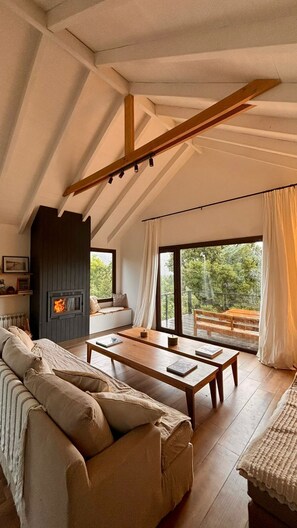 Une chambre confortable aménagée en mezzanine, avec une cheminée, un canapé, une table à manger et de grandes fenêtres donnant sur l’extérieur.